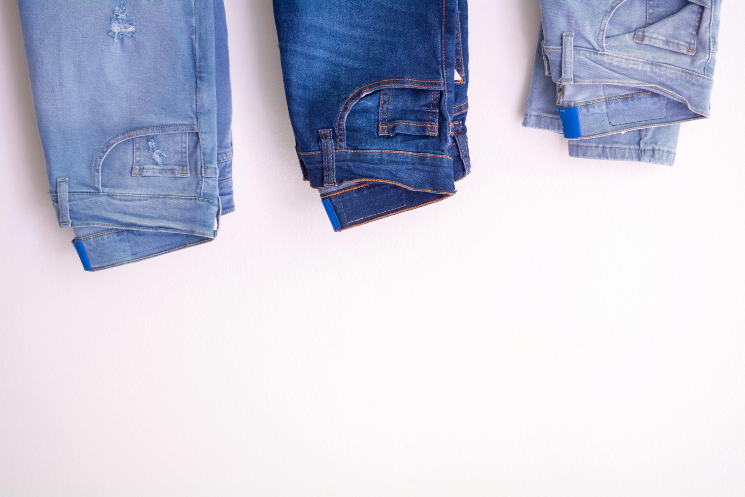 Three pairs of denim jeans neatly folded and hanging against a white backdrop.