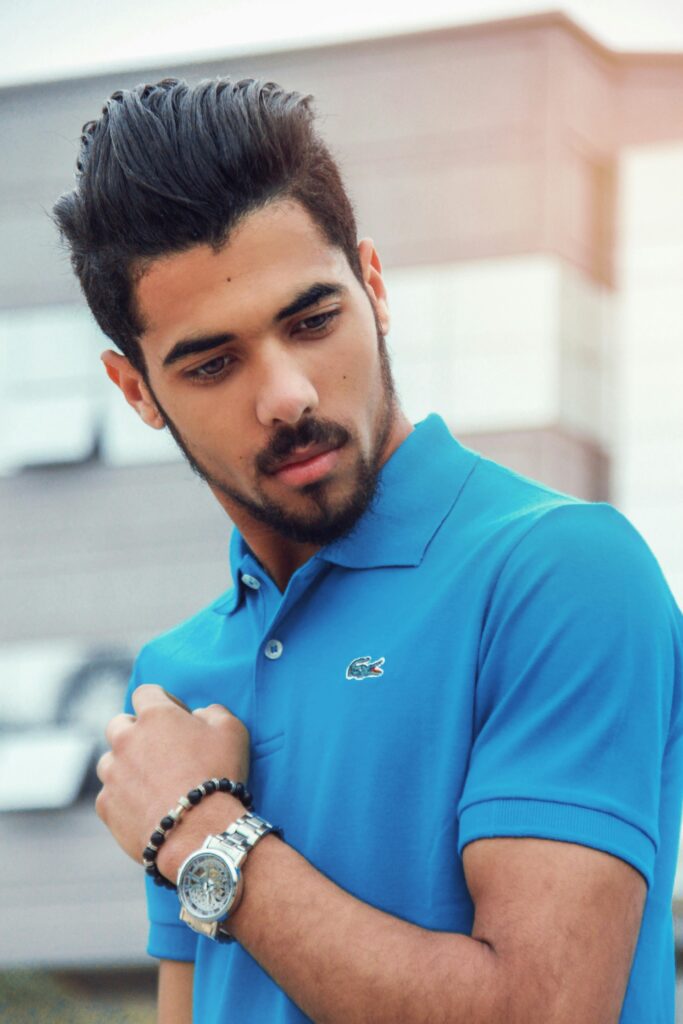 Portrait of a stylish adult male in a blue polo shirt, showcasing modern accessories, set against an urban background.