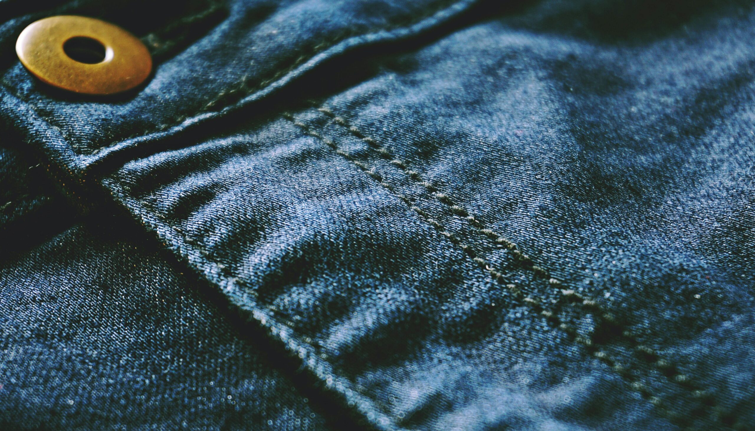 Detailed photo of blue denim fabric showcasing stitches and texture, perfect for fashion design.