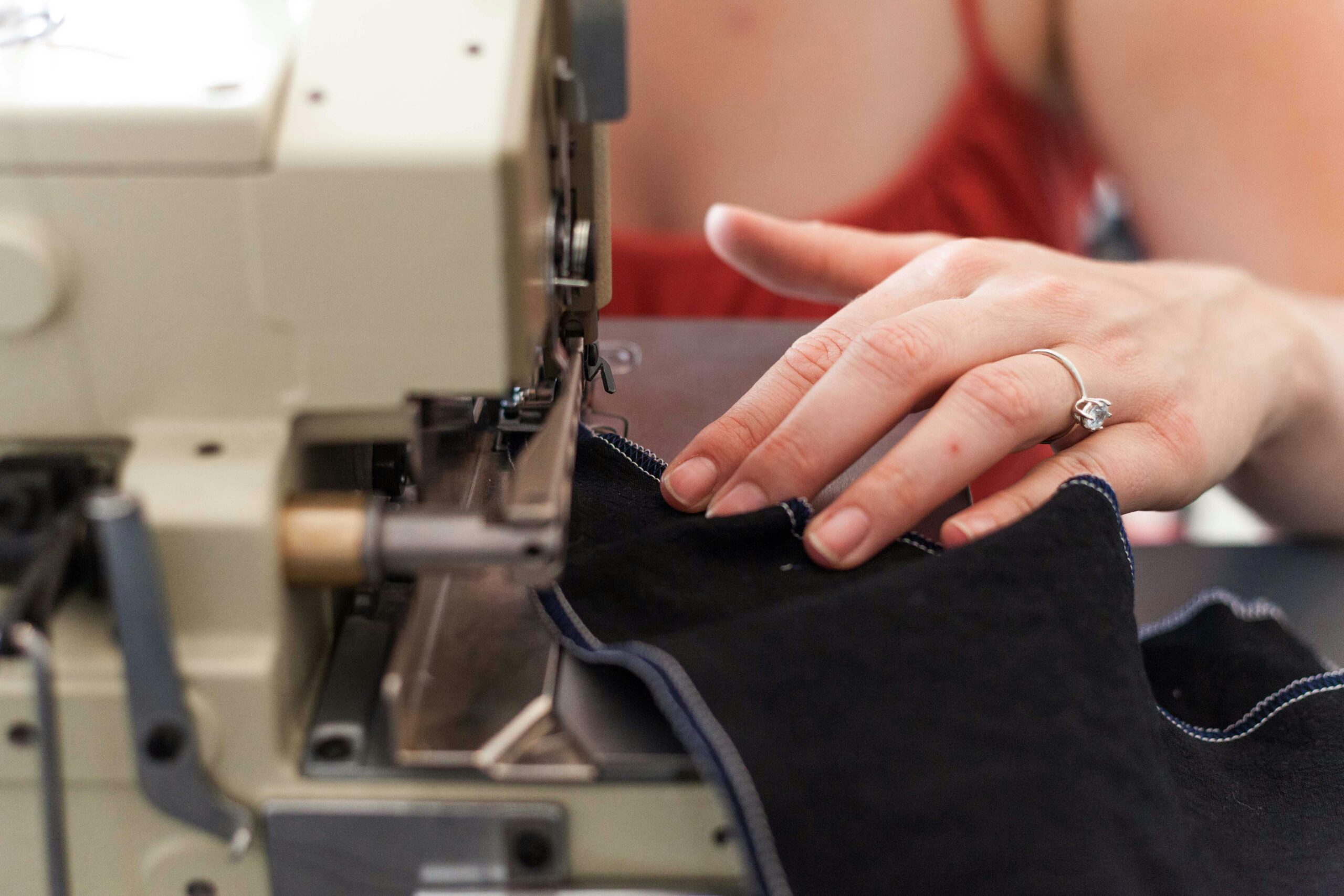 A woman's hand sewing fabric on a machine, with a focus on her diamond ring.